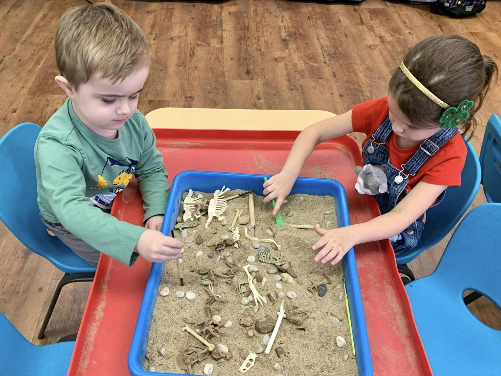 Kids playing in the sand digging for dinosaur bones during dino month.